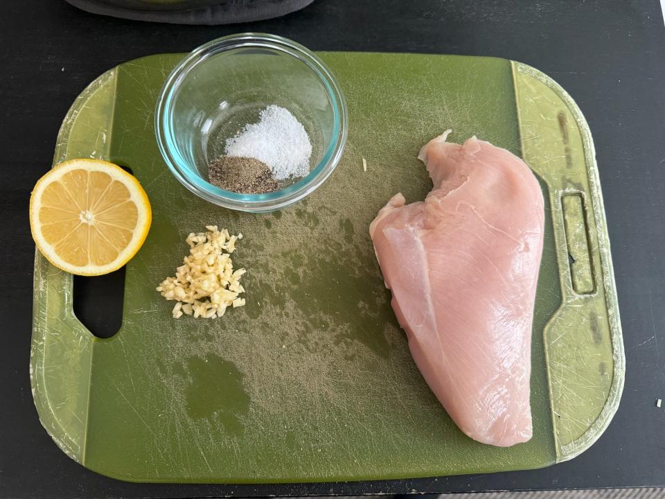 lemon, salt and pepper, and garlic on a cutting board next to a chicken breast