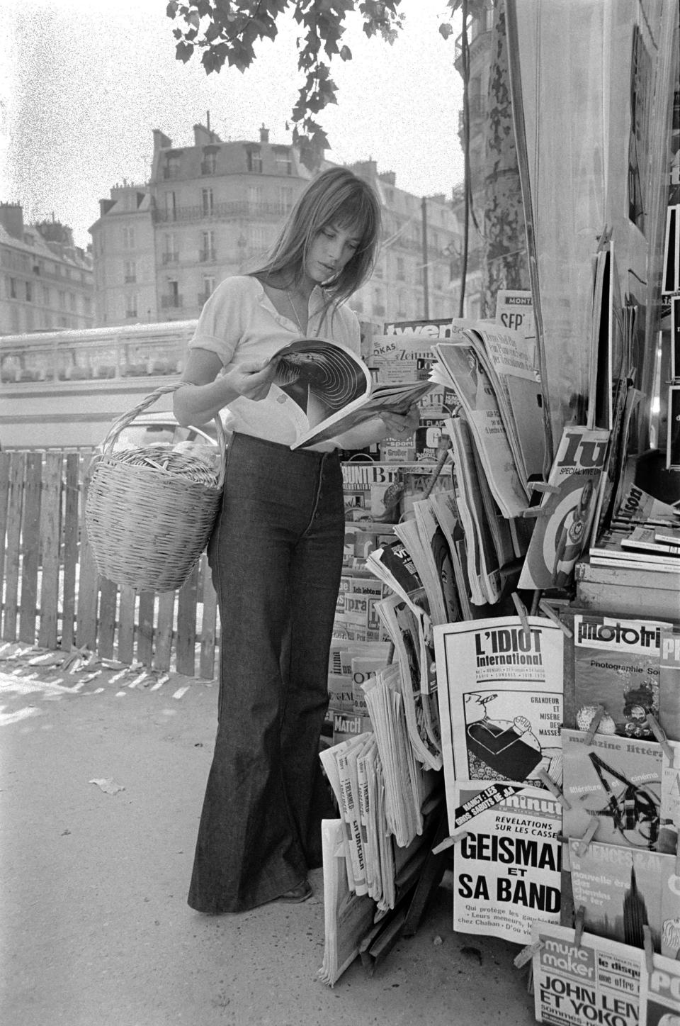 Jane Birkin wears a white blouse and bell bottom jeans and carries a wicker basket bag while shopping in Paris. (Photo: WATFORD/Mirrorpix/Mirrorpix via Getty Images)