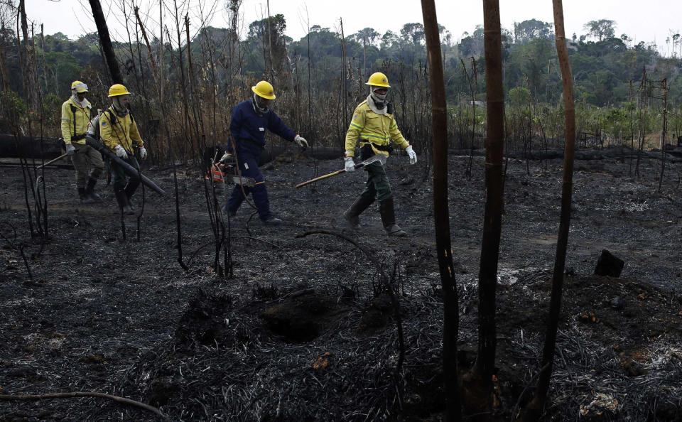 Firefighters walk across charred land to another area as they work to put out fires along the road to Jacunda National Forest in the Vila Nova Samuel region, near the city of Porto Velho in Rondonia state, part of Brazil's Amazon, Sunday, Aug. 25, 2019. Leaders of the Group of Seven nations said Sunday they were preparing to help Brazil fight the fires burning across the Amazon rainforest and repair the damage even as tens of thousands of soldiers were being deployed to fight the blazes that have caused global alarm. (AP Photo/Eraldo Peres)