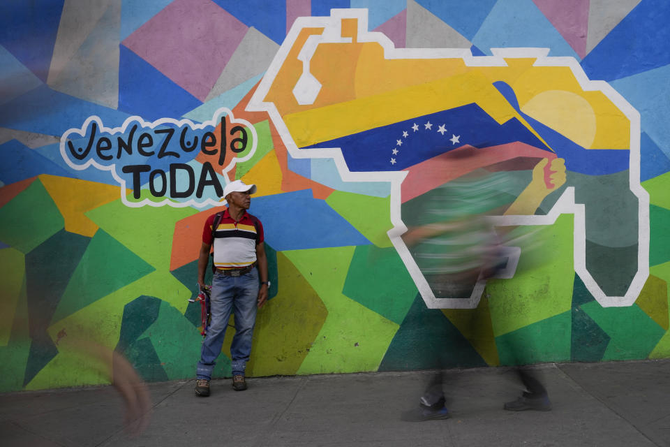 Un hombre vende cables para celulares delante de un mural con un mapa de Venezuela que incluye el territorio de Esequibo, en el vecindario de Petare, en Caracas, Venezuela, el 11 de diciembre de 2023. (AP Photo/Matias Delacroix)