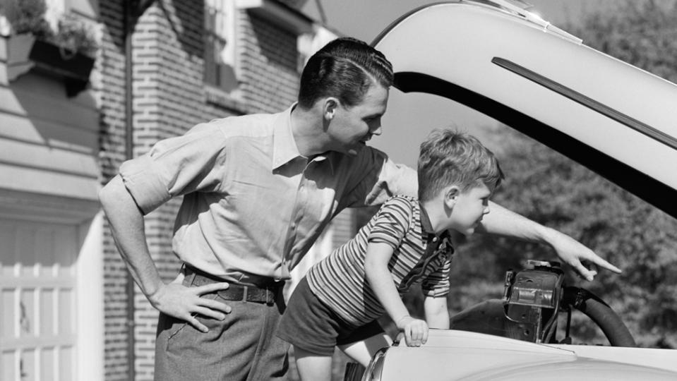 A father and son look under the hood of a car, circa 1940s.