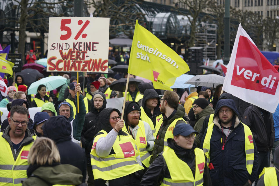 Demonstrators attend a rally of the trade union Ver.di at the Rathausmarkt, in Hamburg, Germany, Thursday, March 23, 2023. German unions are calling on thousands of workers across the country's transport system to stage a one-day strike on Monday that is expected to bring widespread disruption to planes, trains and local transit. Writing on sign at left reads in German; "5% is not appreciation". (Marcus Brandt/dpa via AP)