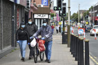 People wearing masks to protect against coronavirus, walk in Melton Road also known as the Golden Mile in Leicester, England, Tuesday June 30, 2020. The British government has reimposed lockdown restrictions in the English city of Leicester after a spike in coronavirus infections, including the closure of shops that don't sell essential goods and schools. (AP Photo/Rui Vieira)