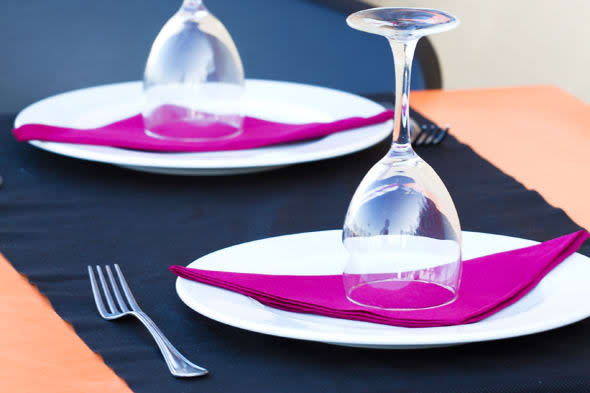 BNKHW4 Outdoor restaurant in Denia, Spain. A table set with black runner, dishes, wine glasses, pink magenta cloth napkins