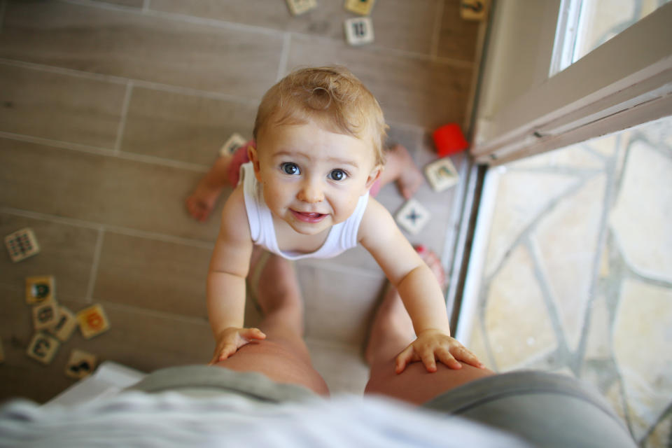 Baby climbing onto adult's knee, looking up at the camera, alphabet blocks scattered around on the floor