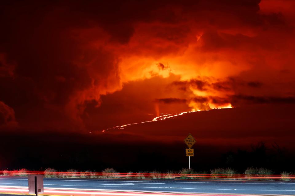 Cars drive down Saddle Road as Mauna Loa erupts in the distance, Monday, November 28, 2022, near Hilo, Hawaii.