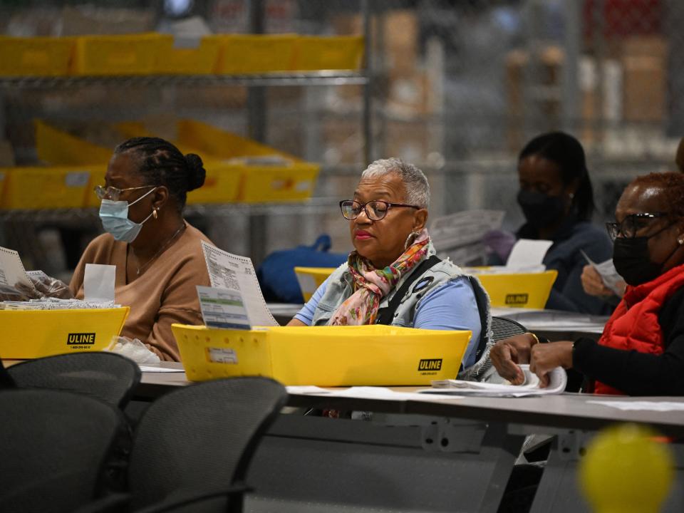 poll workers going through ballots while seated in warehouse