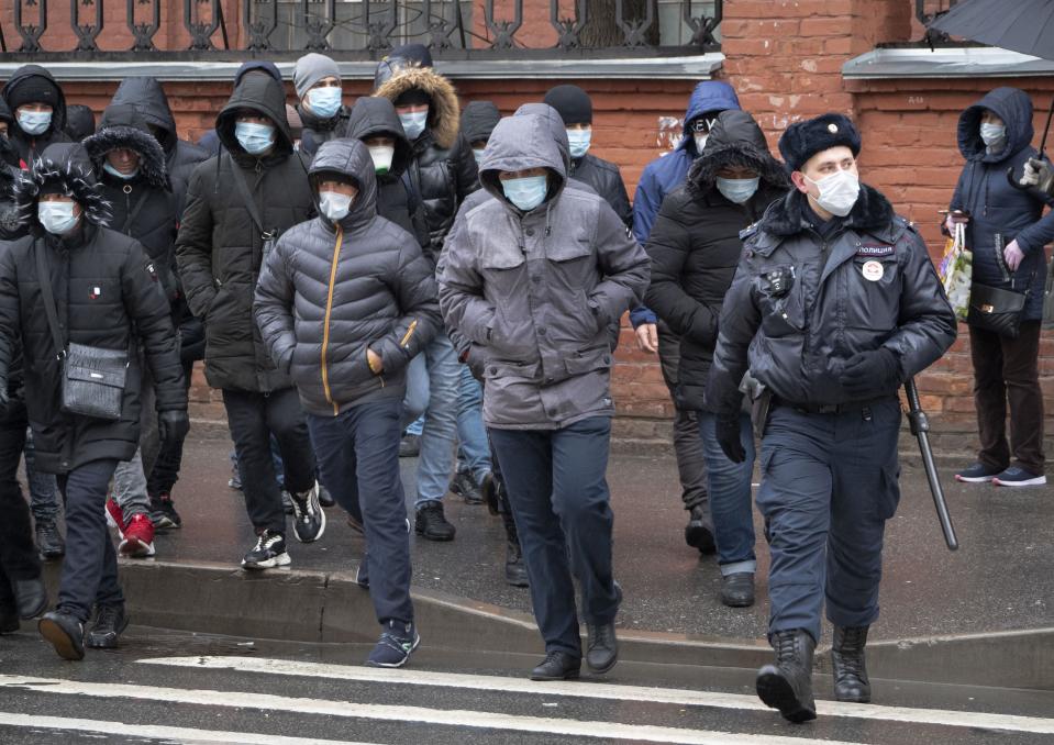 A policeman, foreground right, accompanies a group of migrant laborers, who came to renew work permits, to a migration center in St.Petersburg, Russia, Thursday, April 2, 2020. President Vladimir Putin on Thursday ordered most Russians to stay off work until the end of the month as part of a partial industrial shutdown to curb the spread of the coronavirus. The new coronavirus causes mild or moderate symptoms for most people, but for some, especially older adults and people with existing health problems, it can cause more severe illness or death. (AP Photo/Dmitri Lovetsky)