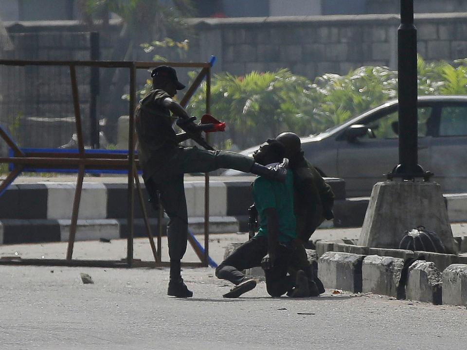 A police officer kicks a protester being detained by Lekki toll gate in Lagos on WednesdayAP