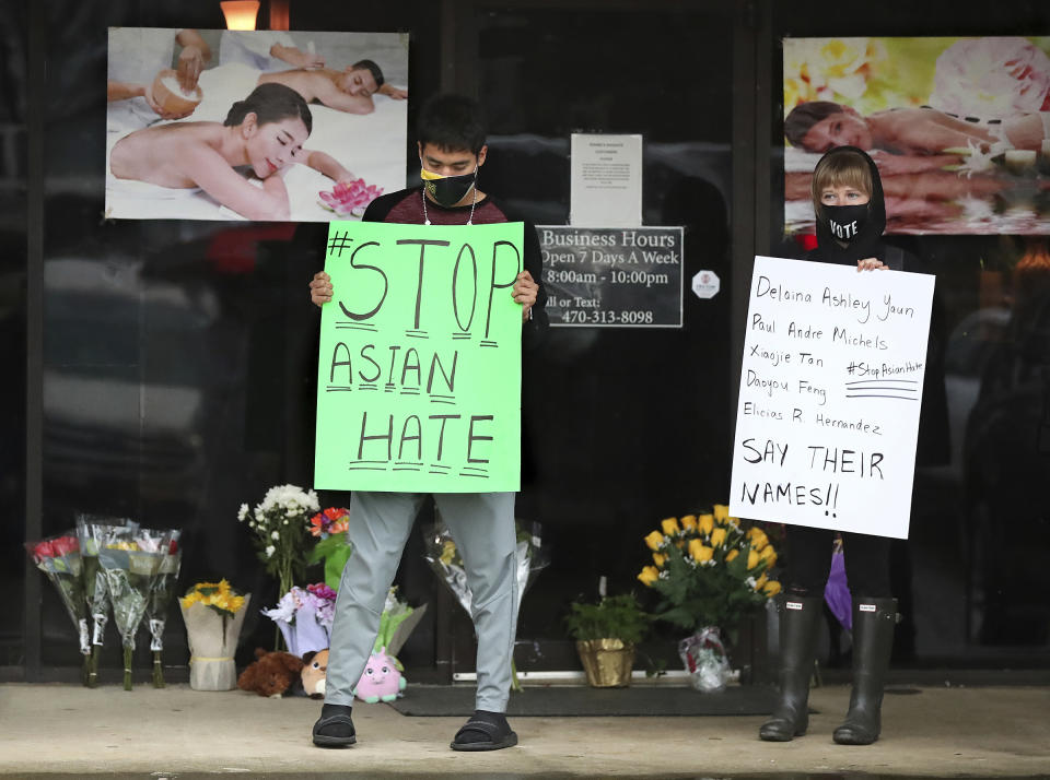 After dropping off flowers Jesus Estrella, left, and Shelby S., right, stand in support of the Asian and Hispanic community outside Youngs Asian Massage parlor where four people were killed, Wednesday, March 17, 2021, in Acworth, Ga. A white gunman was charged Wednesday with killing eight people at three Atlanta-area massage parlors in an attack on Tuesday that sent terror through the Asian American community that’s increasingly been targeted during the coronavirus pandemic. (Curtis Compton/Atlanta Journal-Constitution via AP)