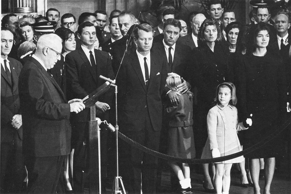 Chief Justice of the United States Earl Warren reads his tribute to martyred President John F Kennedy in ceremonies in the rotunda of the US Capitol, Washington DC, November 24, 1963. The late President's casket had been moved from the White House to the Capitol to permit the public to pay its last respects. Jacqueline Kennedy stands at the right, holding daughter Caroline's hand. Pictured are, from left, Senator Mike Mansfield, Stephen Smith, a brother-in-law of the late President, President Johnson, behind Robert Kennedy, Peter Lawford, comforting 7-year-old daughter Sydney, Mrs Lawford, President Kennedy's sisters Patricia, Mrs Kennedy, and Caroline. (Photo by PhotoQuest/Getty Images)<span class="copyright">Getty Images</span>