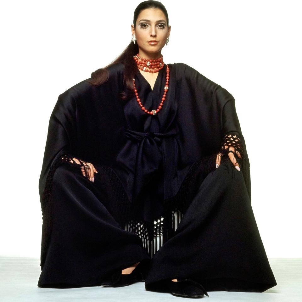 Valentino’s soft-falling black poncho of heavy silk crepe dripping with knotted fringe, sashed in front over flaring pants—looped and jeweled with ropes and ropes of coral beads. Fabric by Forneris. Jewelery by Coppola e Toppo; shoes by Dal Co’, for Valentino. Worn by Benedetta Barzini.