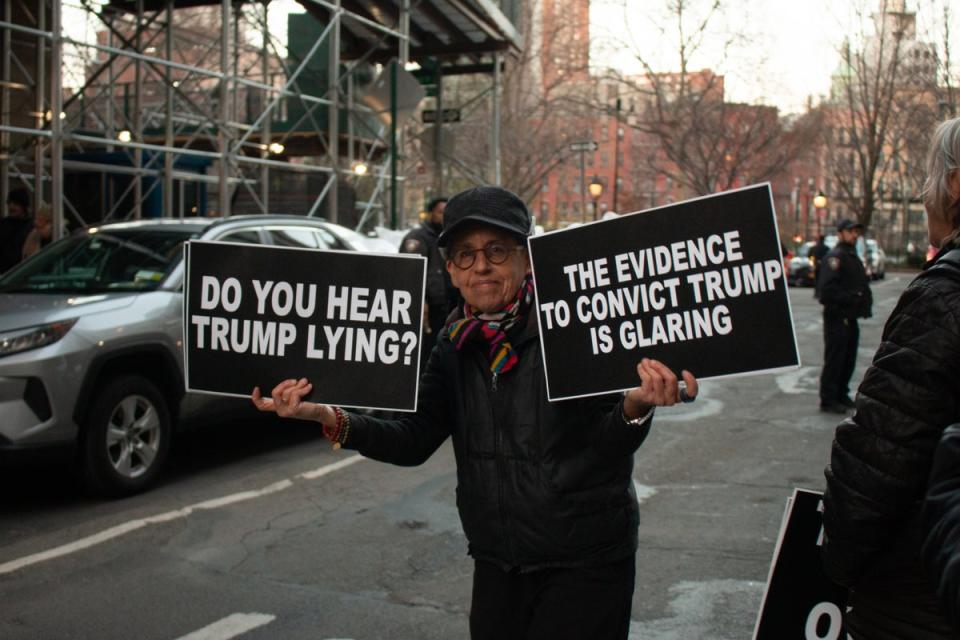 A protester holds up signs in support of the Trump indictment (Ariana Baio / The Independent)