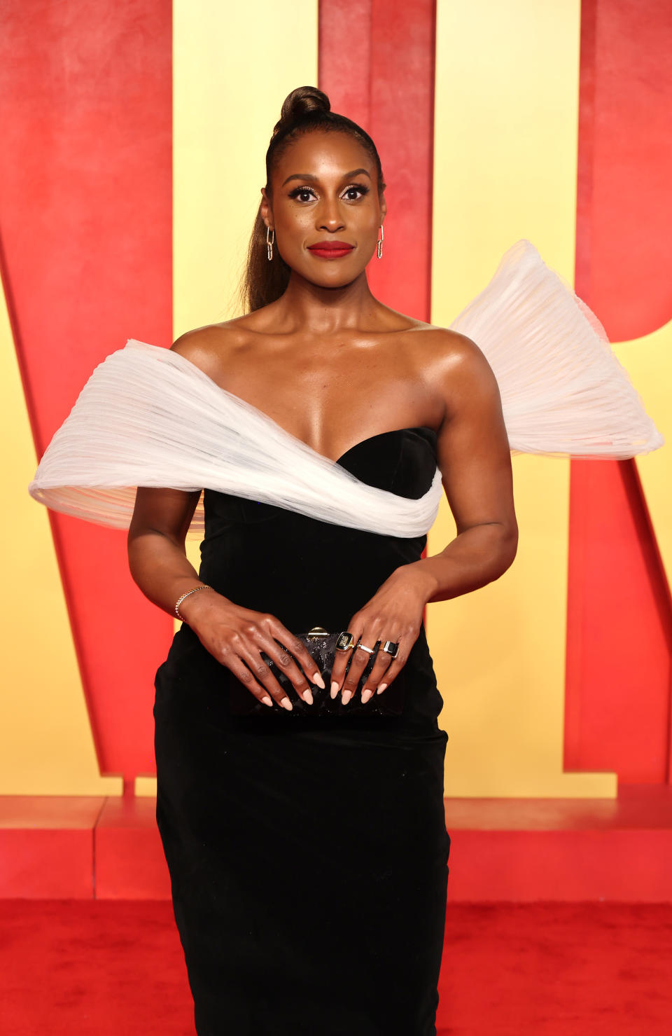 Person on red carpet in black dress with dramatic white shoulder detail, standing, facing camera