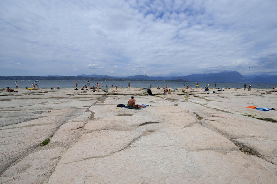 People sunbath on the peninsula of Sirmione, on Garda lake, Italy, Friday, Aug. 12, 2022. Lake Garda water level has dropped critically following severe drought resulting in rocks to emerge around the Sirmione Peninsula. (AP Photo/Antonio Calanni)