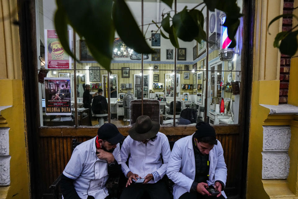 Barberos de la Peluquería Francesa, sentados fuera de su trabajo en el barrio de Yungay en Santiago, Chile, el 6 de junio de 2024. Yungay es un barrio donde se combinan edificios históricos, fachadas barrocas y modernos restaurantes. Se ha convertido también en una zona donde es frecuente ver a personas sin hogar. (AP Foto/Esteban Félix)