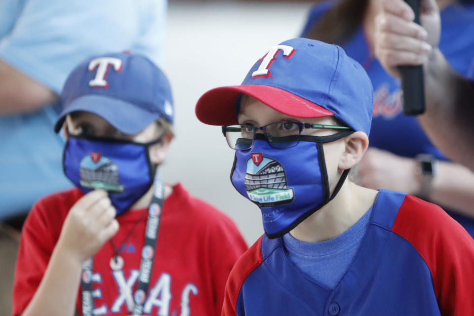 FILE - In this June 1, 2020, file photo, Gavin Bollmer, left, and his buddy, Austin LaFountain, wear Globe Life Field masks as they tour the home of the Texas Rangers baseball team in Arlington, Texas. Many organizations are trying to bridge the budget gap from the coronovirus through enhanced sponsorship sales, such as temporary billboards that could be stretched over unsold sections of seats. Teams and leagues are selling branded face masks and other personal protective equipment. Almost all of them are trying to engage fans in new and creative ways. It won't come close to making up the budget shortfall, but the hope is to survive long enough for sports to return to normal. (AP Photo/LM Otero, File)