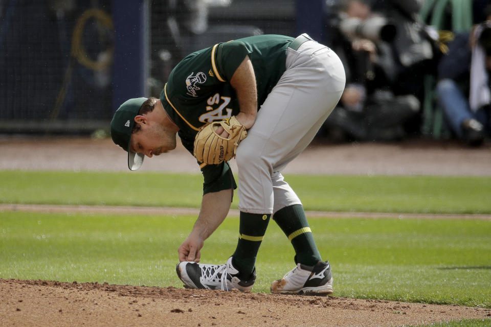 Oakland Athletics starting pitcher Daniel Mengden cleans mud off his shoes as he throws during the first inning of a spring training baseball game against the Seattle Mariners, Friday, Feb. 22, 2019, in Peoria, Ariz. (AP Photo/Charlie Riedel)