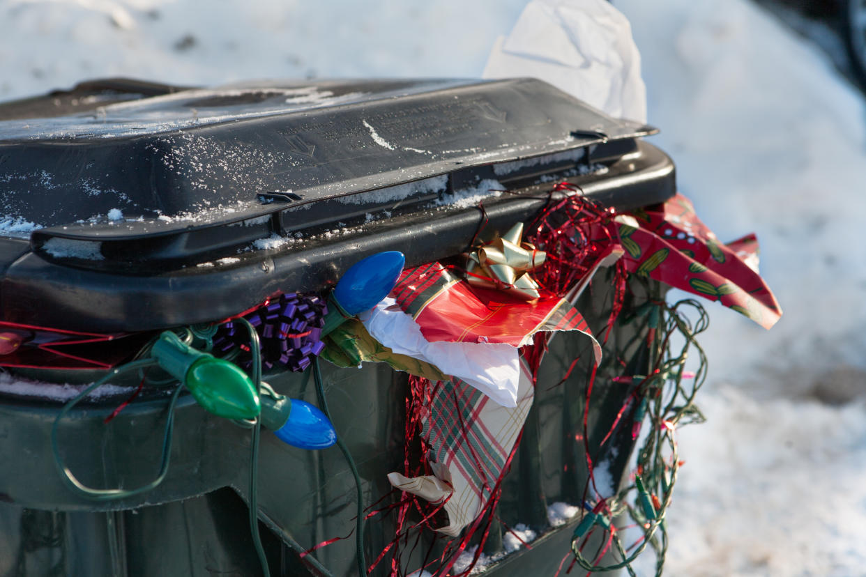 a large plastic trashbin overflowing with garbage and discarded Christmas paper lights bows etc