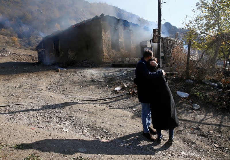 Residents hug as they stand near a house set on fire by departing Ethnic Armenians in the village of Cherektar, in the region of Nagorno-Karabakh