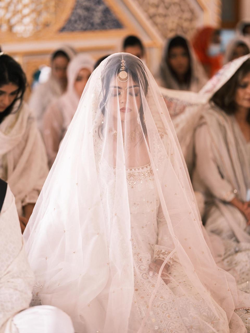 A bride closes her eyes during her wedding ceremony. A veil partially obscures her face.