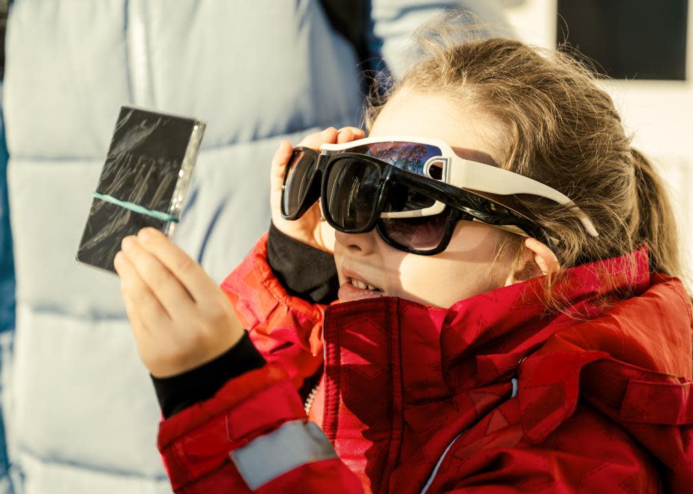 Small child wearing three pairs of sunglasses, watching the solar eclipse through a filter.