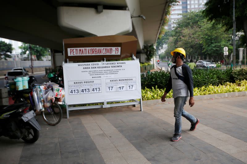 A worker wearing a protective mask walks past a mockup coffin of a COVID-19 victim displayed on the sidewalk of a road to encourage adherence to health protocols, as the coronavirus disease (COVID-19) outbreak continues in Jakarta