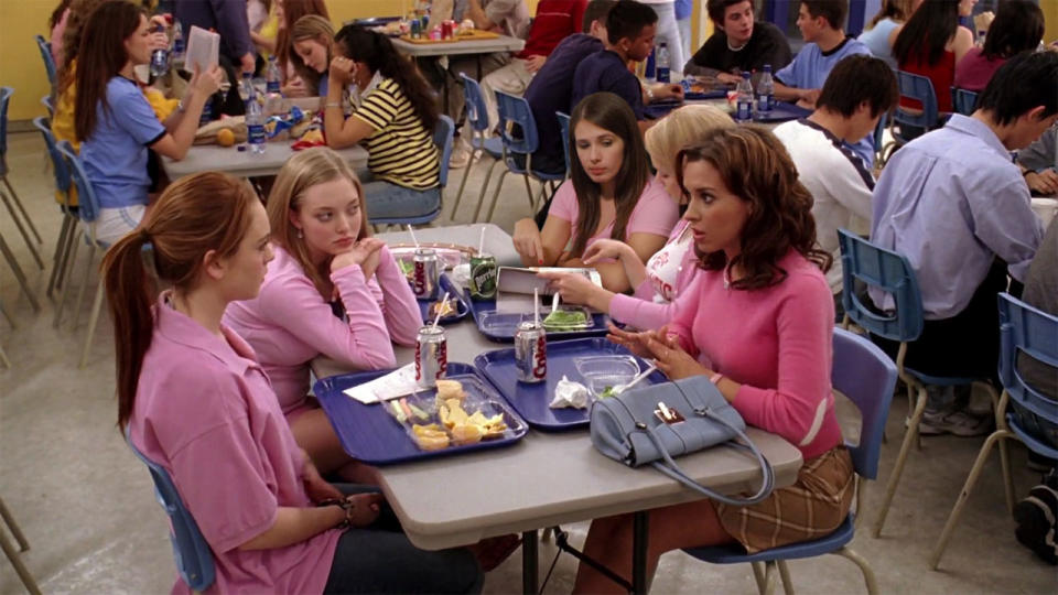 Lindsay Lohan, Rachel McAdams, Amanda Seyfried, and Lacey Chabert are sitting at a high school cafeteria table, all wearing pink tops, talking, and eating lunch