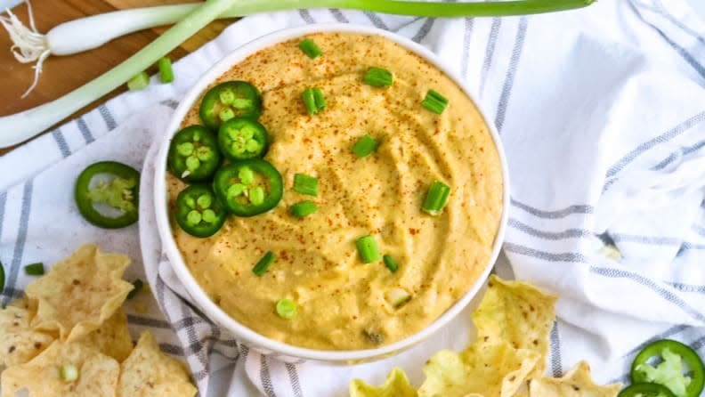 Vegan queso dip topped with jalapeños and accompanied by tortilla chips