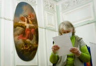 A woman wearing a face mask to protect against coronavirus infection reads her ballot at a polling station in St. Petersburg, Russia, Wednesday, July 1, 2020. The vote on the constitutional amendments that would reset the clock on Russian President Vladimir Putin's tenure and enable him to serve two more six-year terms is set to wrap up Wednesday. (AP Photo/Dmitri Lovetsky)