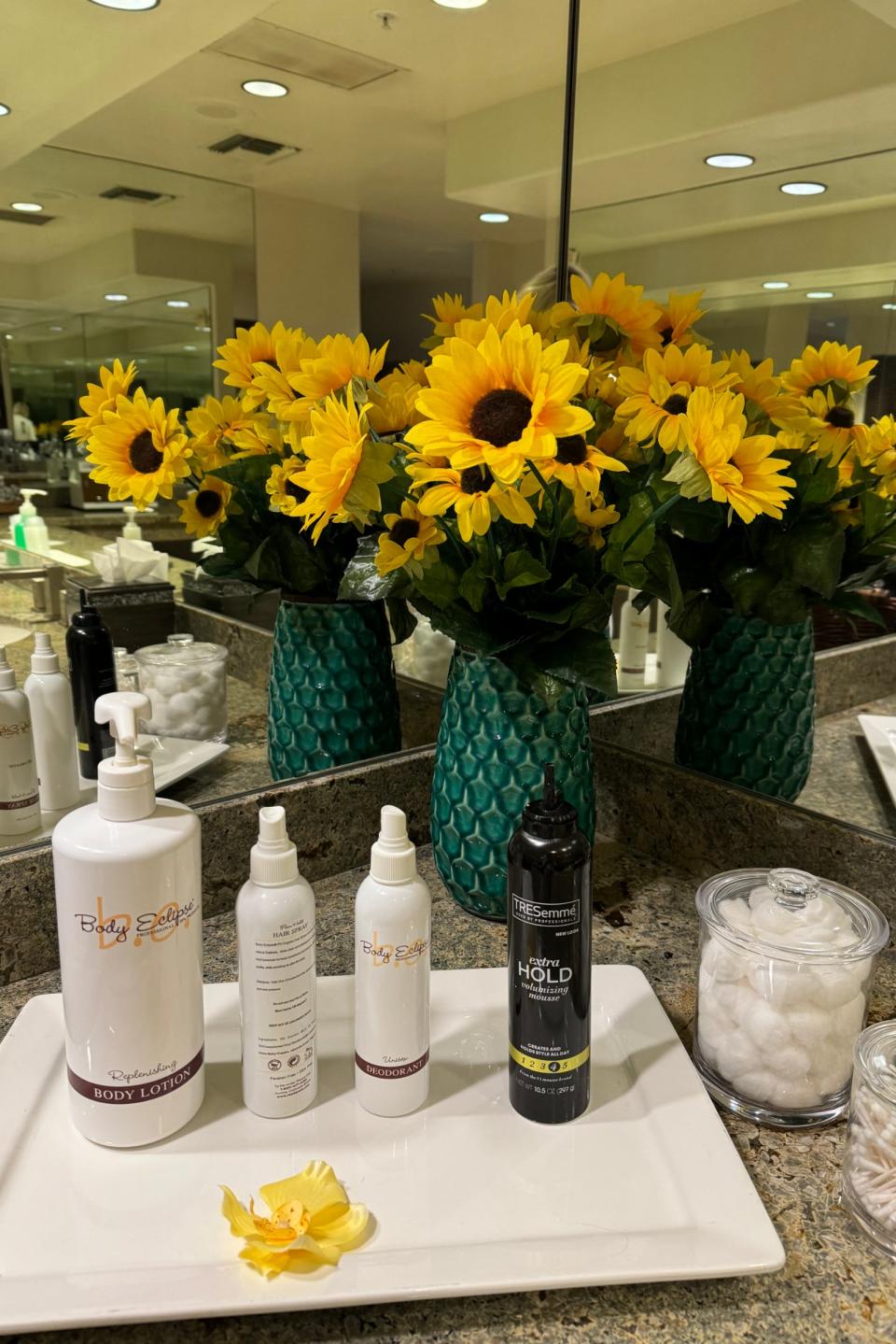 Sunflowers in a vase on a bathroom counter with various toiletry items around