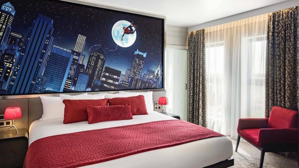 A hotel room with red pillows and a red blanket with a picture of Spider-Man behind the bed