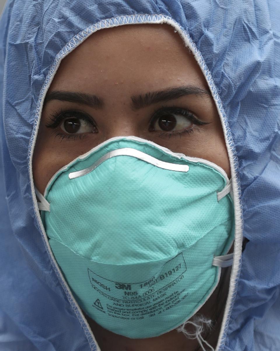 A nurse, dressed in protective gear as a precaution against the spread of the new coronavirus, stands by as she waits to check the temperatures of commuters at a checkpoint outside a bus station in Soacha, on the outskirts of Bogota, Colombia, Wednesday, April 1, 2020. (AP Photo/Fernando Vergara)