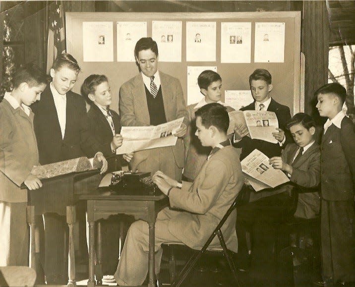 In one of his early years on the faculty of Gibbons Hall, adviser Joe Lalley and the Gibbons Hall Class of 1952 review the latest issue of The Cardinal.  To the left of Lalley are an unidentified student, Brad Moore, and Wriston Thompson.  At right are Tom King, Kerry Rudy, Larry Redmond (seated), and Leicester Chapman.  Dick Arnold sits at the typewriter, perhaps preparing the lead story for the next issue.