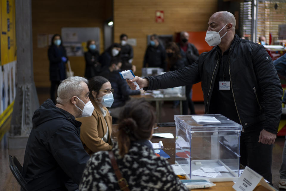 A man working at a polling station set up in a market, is taken the temperature during the regional Catalan election in Barcelona, Spain, Sunday, Feb. 14, 2021. Over five million voters are called to the polls on Sunday in Spain's northeast Catalonia for an election that will measure the impact of the coronavirus pandemic on the restive region's secessionist movement. (AP Photo/Emilio Morenatti)