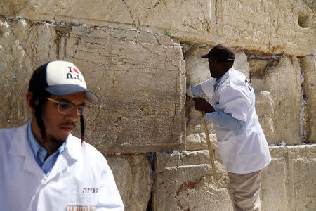 Men clear notes placed in the cracks of the Western Wall, Judaism's holiest prayer site, to create space for new notes ahead of the Jewish holiday of Passover, in Jerusalem's Old City, March 20, 2018. REUTERS/Ammar Awad