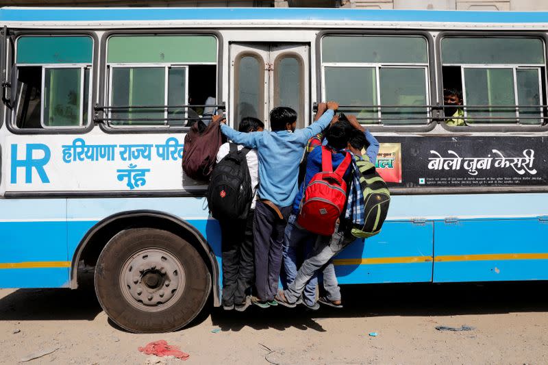 Migrant workers hang on to a door of their moving bus as they return to their villages, during a 21-day nationwide lockdown to limit the spreading of coronavirus disease (COVID-19), in Ghaziabad