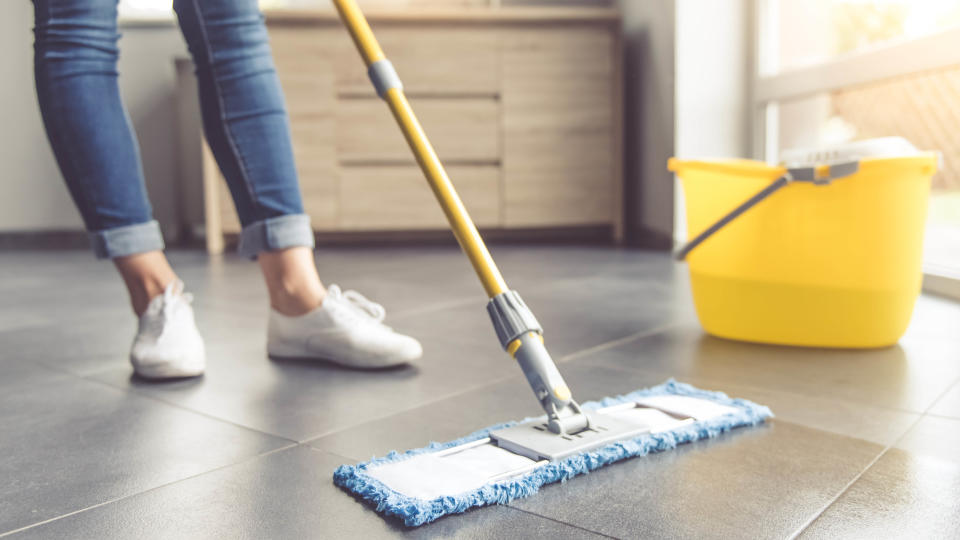 Someone mopping a tiled floor with a flat mop and yellow bucket