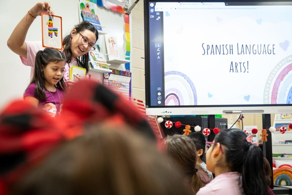 Tuloso-Midway Primary School first grade teacher Raquel Covarrubias holds a card with a letter from the Spanish alphabet over student Mackenzie Armendariz's head. Fellow classmates enunciate to help Armendariz guess what's on the card, Dec. 8, 2023, in Corpus Christi.