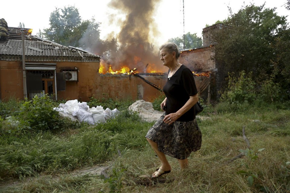 ARCHIVO - Una mujer corre desde una casa incendiada tras ataques en Donetsk, en territorio bajo control de la República Popular de Donetsk, en el este de Ucrania, el vienes 3 de junio de 2022. (AP Foto/Alexei Alexandrov, archivo)