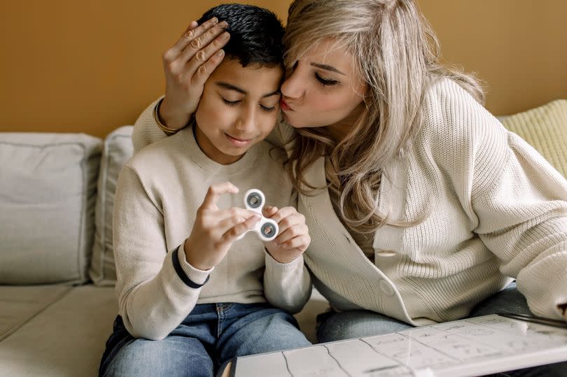 Mother kissing son while teaching at home - stock photo