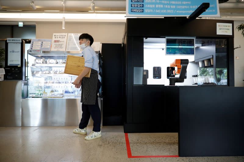 An employee stands next to a barista robot that takes orders, makes coffee and brings the drinks straight to customers in Daejeon