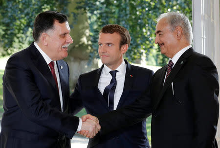 French President Emmanuel Macron stands between Libyan Prime Minister Fayez al-Sarraj (L), and General Khalifa Haftar (R), commander in the Libyan National Army (LNA), who shake hands after talks over a political deal to help end Libya’s crisis in La Celle-Saint-Cloud near Paris, France, July 25, 2017. REUTERS/Philippe Wojazer