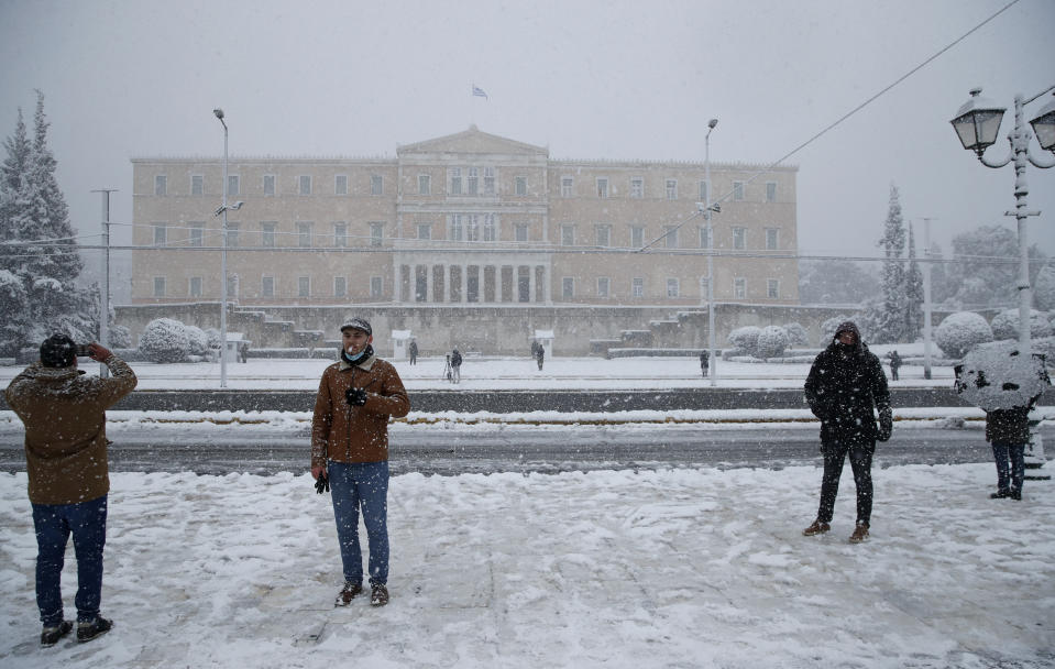 People take photographs as snow falls in front of the Greek parliament in Athens, Tuesday, Feb. 16, 2021. A cold weather front has hit Greece, sending temperatures plunging from the low 20s Celsius (around 70 Fahrenheit) on Friday to well below freezing on Tuesday, and heavy snowfall in central Athens. (AP Photo/Thanassis Stavrakis)