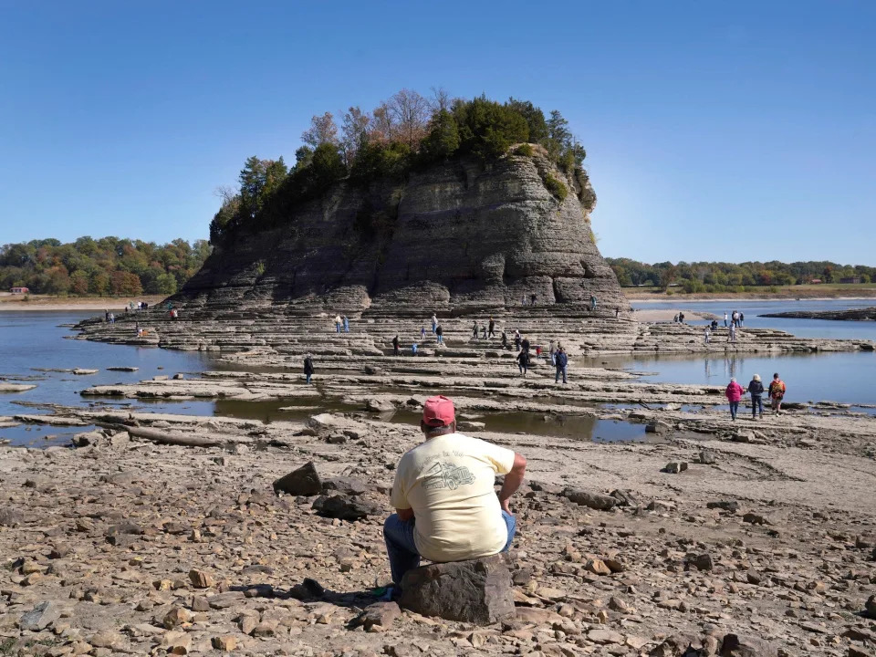 man sits on rock watches people walk across exposed river bottom to big rock island in the mississippi river