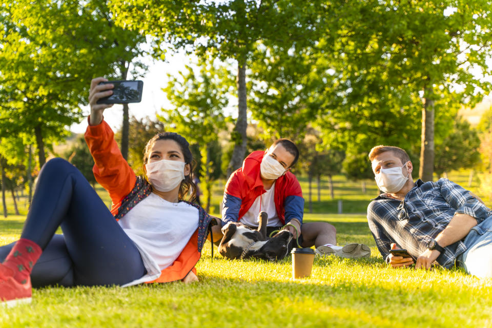 Cheerful university student taking selfie with friends sitting on grass