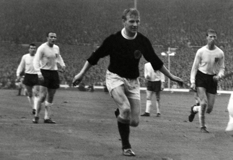 In action for Scotland during the 2-2 draw against England at Wembley in 1965, watched by Jack Charlton, right - Colorsport/Shutterstock