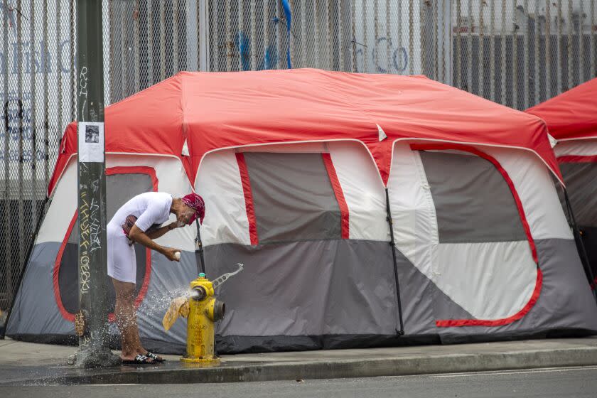 Los Angeles, CA - June 22: Yolanda Robins, 50, washes her face in water flowing from a fire hydrant in a skidrow on Wednesday, June 22, 2022, in Los Angeles, CA. In January, Yolanda Robins's dream was finally coming true. After three decades of living amid the squalor of Skid Row, occasionally punctuated by short stays in hotel rooms or shelters, she was approved to move into an apartment where she could begin to rebuild her life at 50 years old with help from a federal housing subsidy program. She is still living on the street. (Francine Orr / Los Angeles Times)