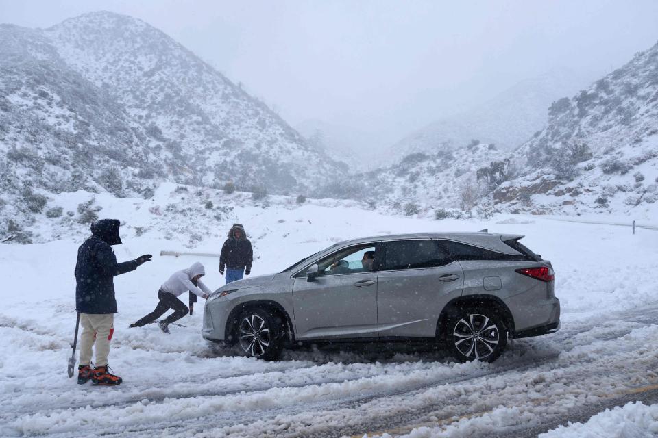 A person helps push out a vehicle that became stuck in the snow on a roadway in the San Gabriel Mountains in the Angeles National Forest, California, on Feb. 24, 2023. - Californians more used to flip flops and shorts were wrapping up warm Thursday as a rare winter blizzard, the first in more than 30 years, loomed over Los Angeles, even as the US East Coast basked in summer-like temperatures.