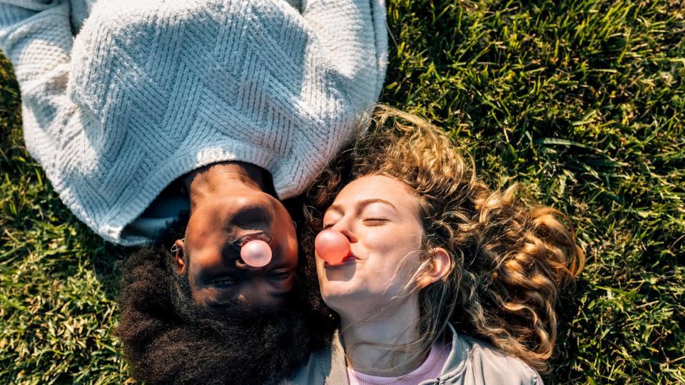 Dos mujeres comiendo chicle y sonriendo acostadas en el césped